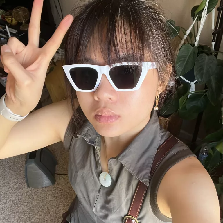 Person in tennis dress with white sneakers and white cat eye sunglasses making a peace sign