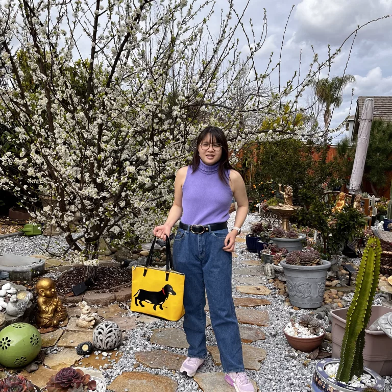 Woman in purple sleeveless knit with straight-leg denim trousers and yellow bag