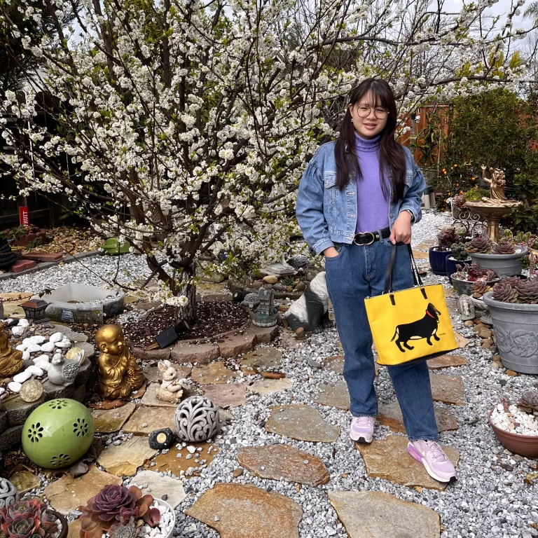 Woman in denim jacket and purple sleeveless knit with straight-leg denim trousers and yellow bag