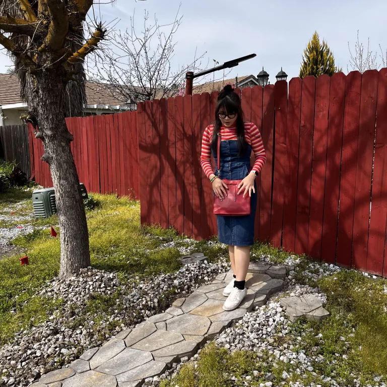 Woman in striped turtleneck underneath denim dress with white sneakers and red purse