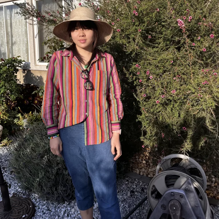 Woman in straw hat with blue jean capris and half tucked rainbow striped dress shirt